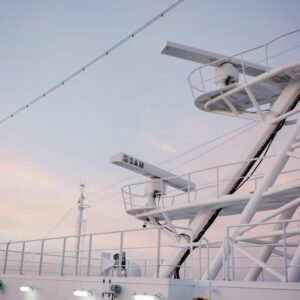 Close-up of a modern ship's radar tower and telecommunications equipment against a pastel sunset sky.
